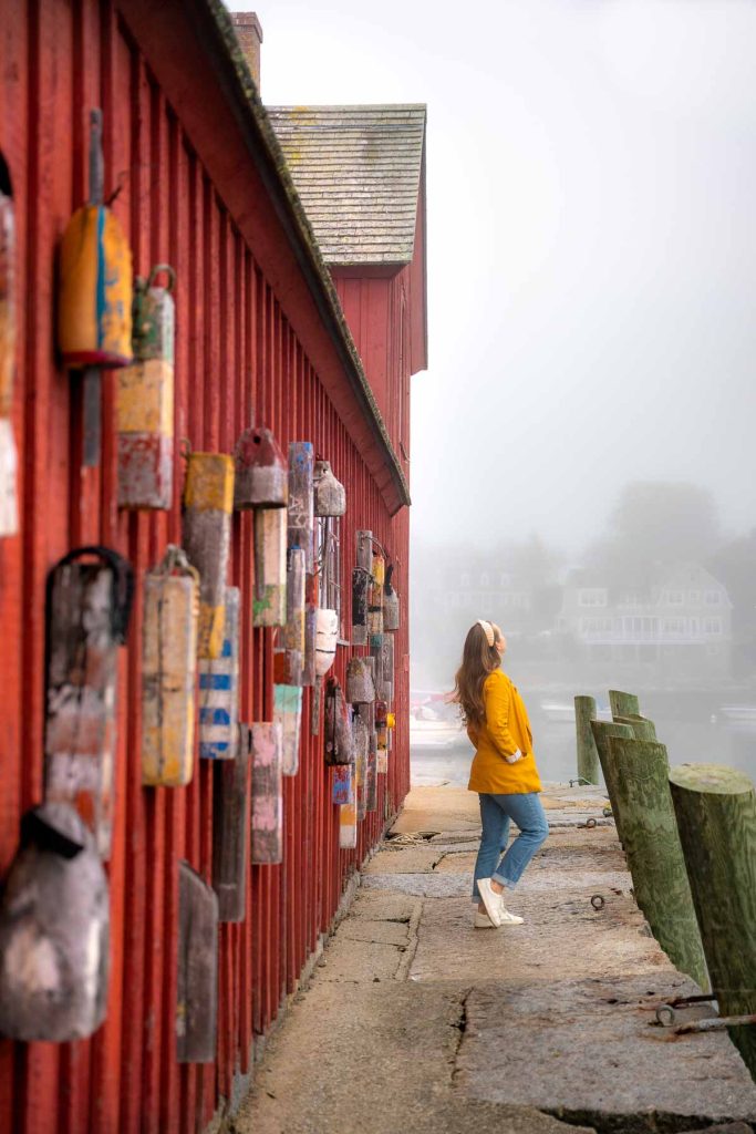 girl in a yellow jacket walking on a pier next to a red building with buoy hanging on it