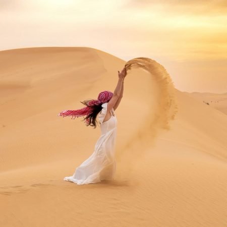 Sam in desert throwing sand over head.