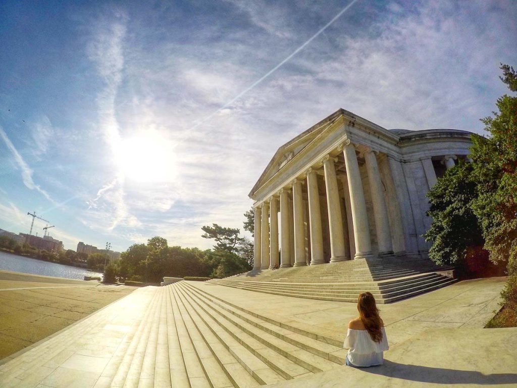 Girl in a white shirt sitting on steps in front of a white column building.