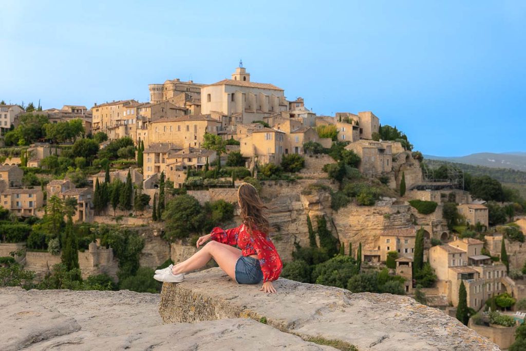Girl in a red long sleeve top sitting on a ledge over looking a medieval town.