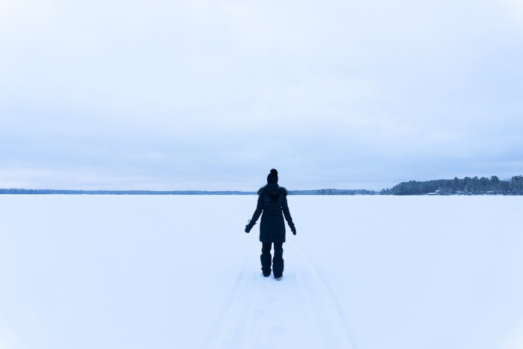 Girl wearing all black winter wear standing in the middle of a white snowy field.