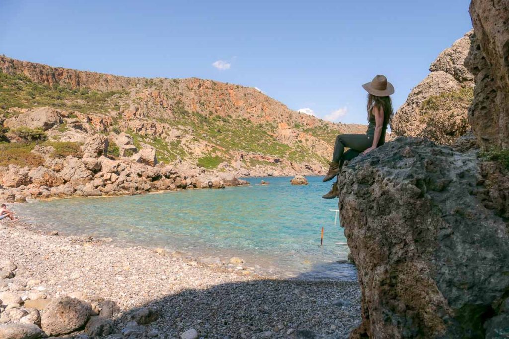 Girl sitting on a rock ledge overlooking a pebbly beach.