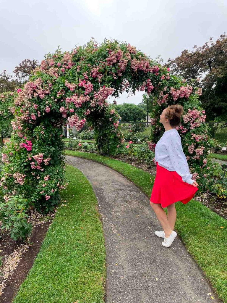 Girl in a red skirt walking under a pink rose arch.