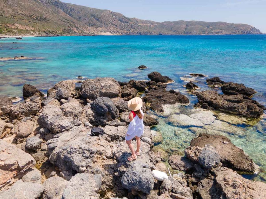 girl standing on rocks overlooking the blue ocean.