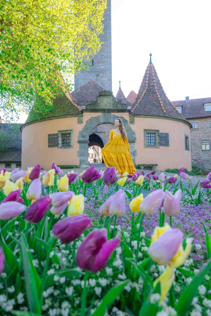 A girl in a yellow dress walking in front of a entrance gate to a small town.