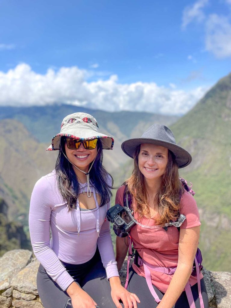 Two girls wearing hats and a camera capture clip sitting on a stone wall.