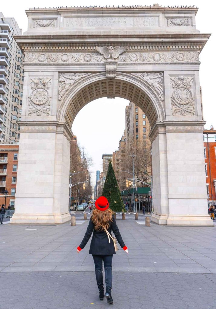 Girl in a red hat standing in front of an archway with a green Christmas tree.